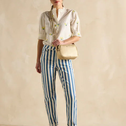 Joules TRENT Womens Cross Body Bag Gold worn by a model in a front view with striped pants and a blouse.