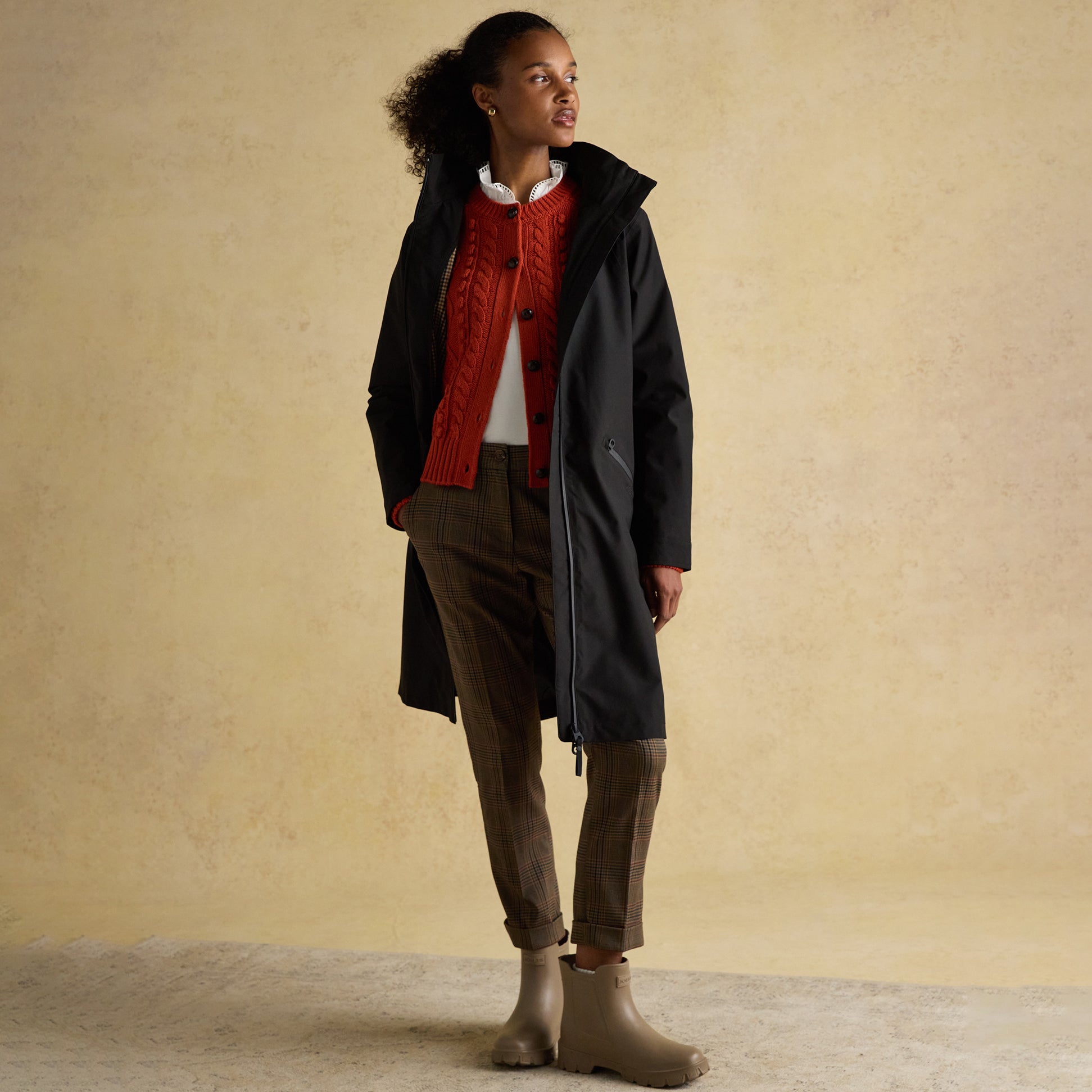 Joules RAINAWAY Womens Lightweight Waterproof Longline Raincoat with Hood Black side view model wearing jacket with red sweater