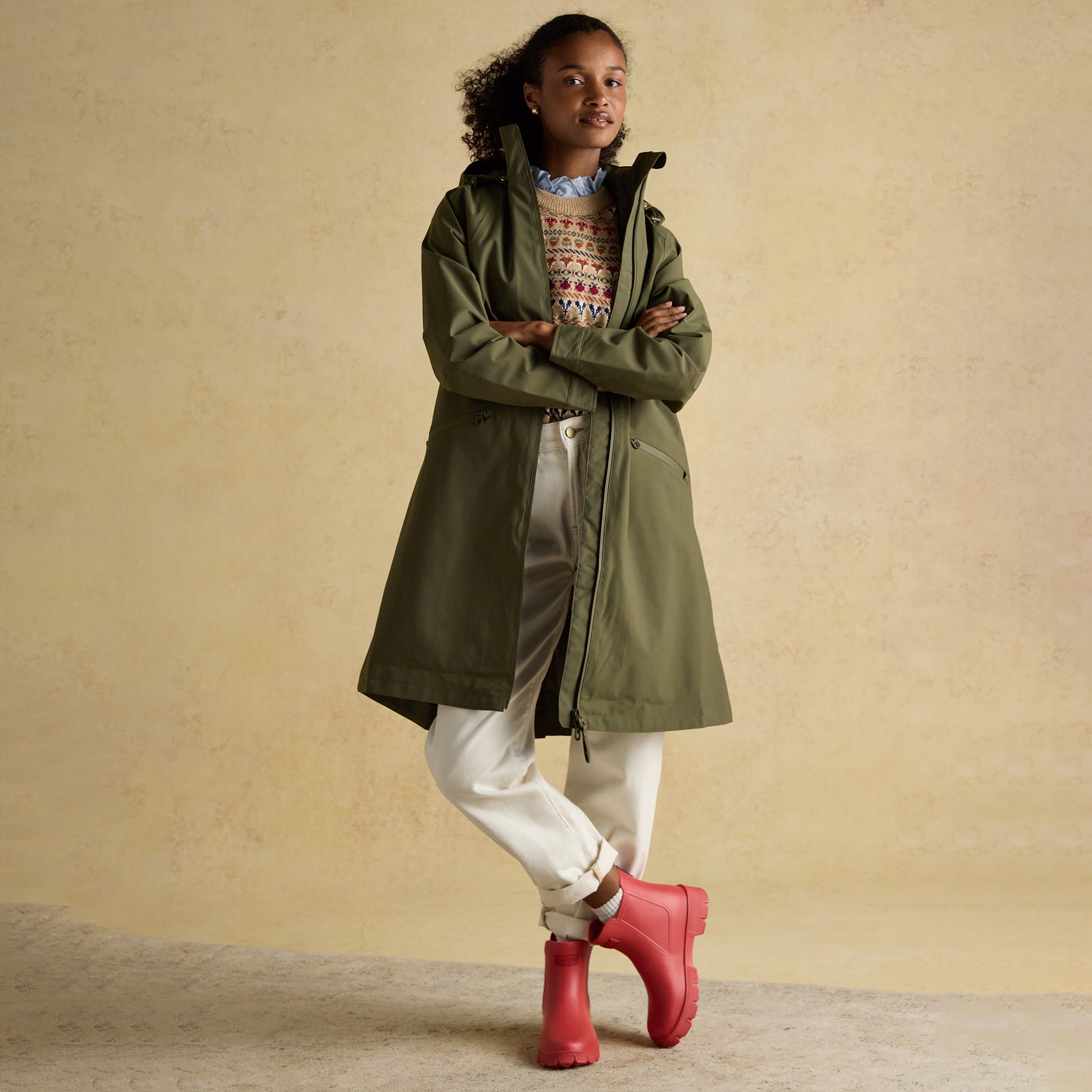 Joules RAINAWAY Womens Lightweight Waterproof Longline Raincoat with Hood Green, side view on model featuring pink rainboots.