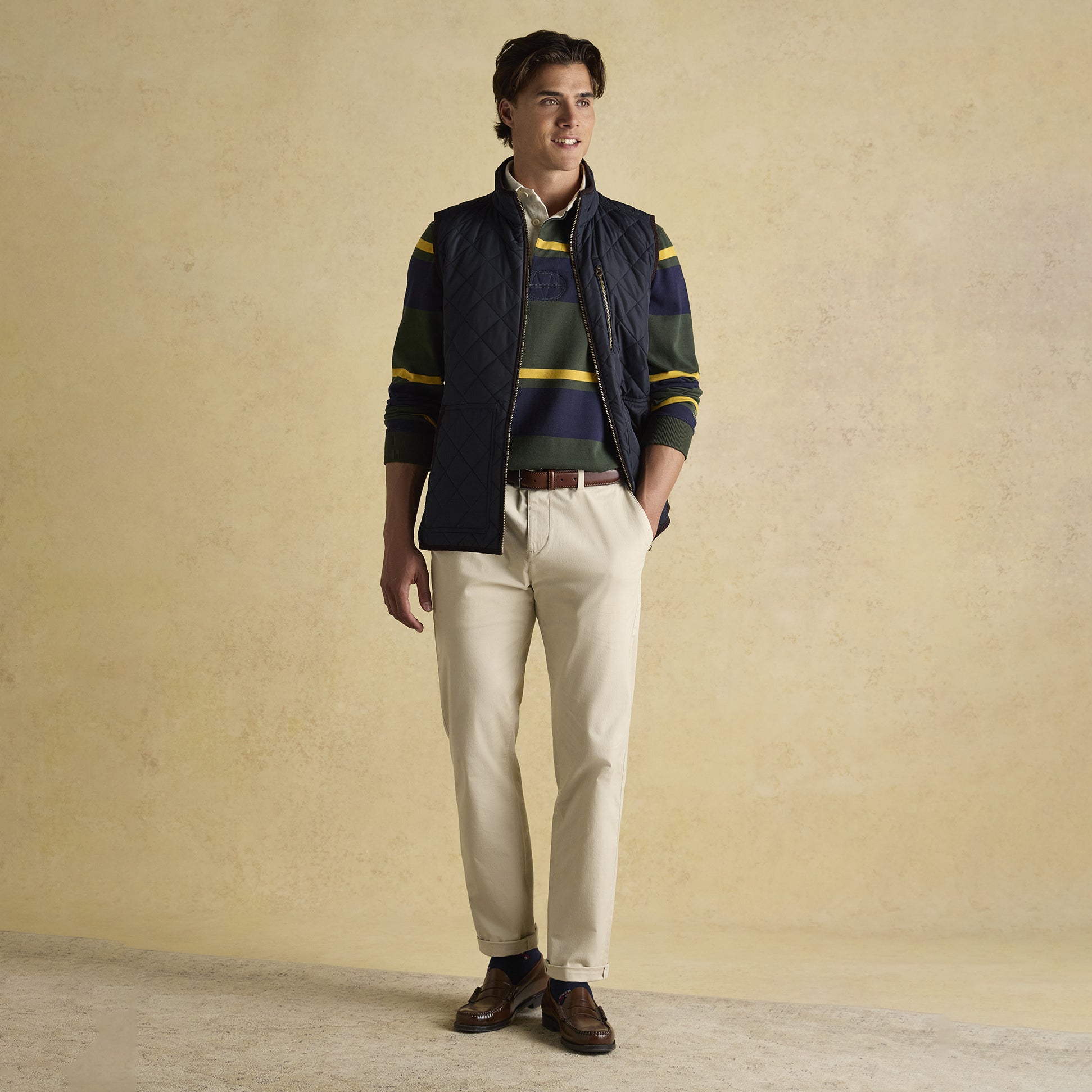 Joules MAYNARD Mens Gilet Navy front view worn over a striped shirt, complemented with cream trousers and brown shoes.