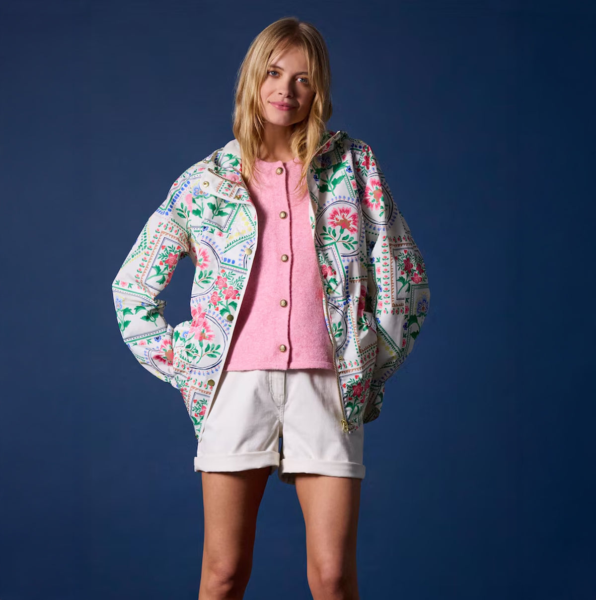 Joules Holt Womens Tile Print Waterproof Packable Raincoat with Hood front view, model wearing with pink top and shorts.