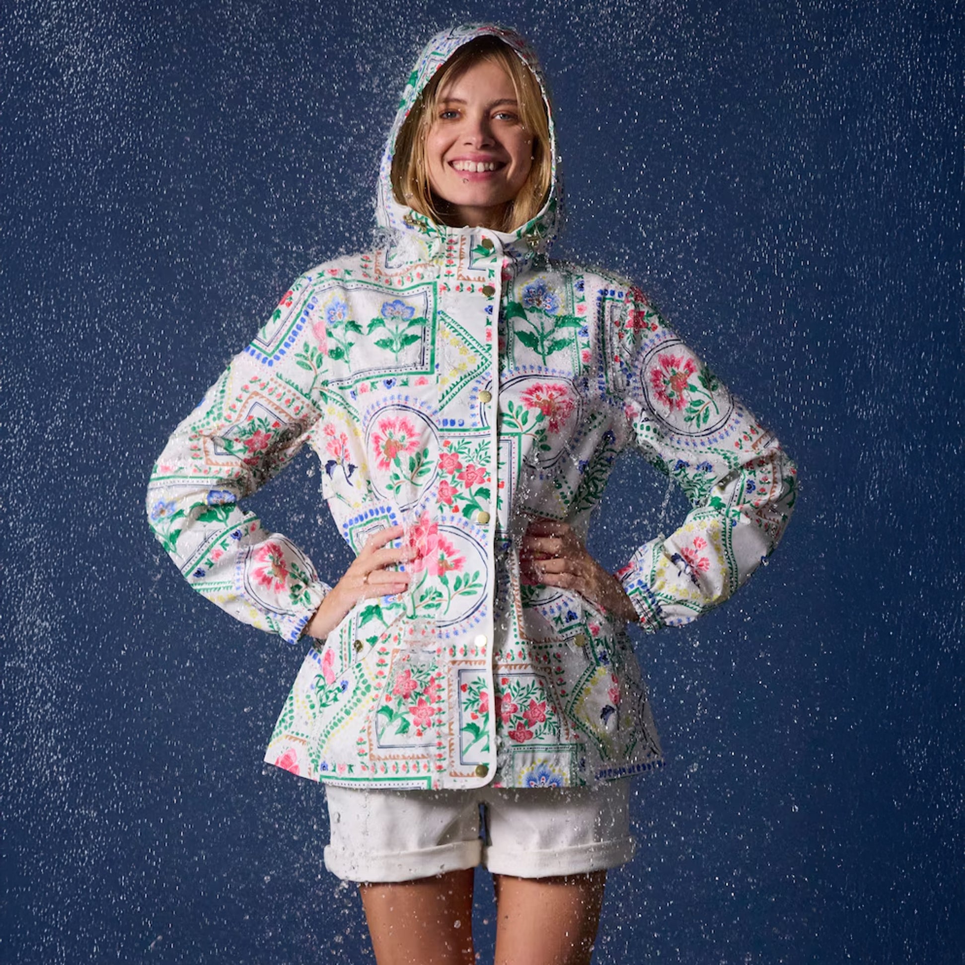 Joules Holt Womens Tile Print Waterproof Packable Raincoat with Hood, front view, model wearing in rain, vibrant floral design.