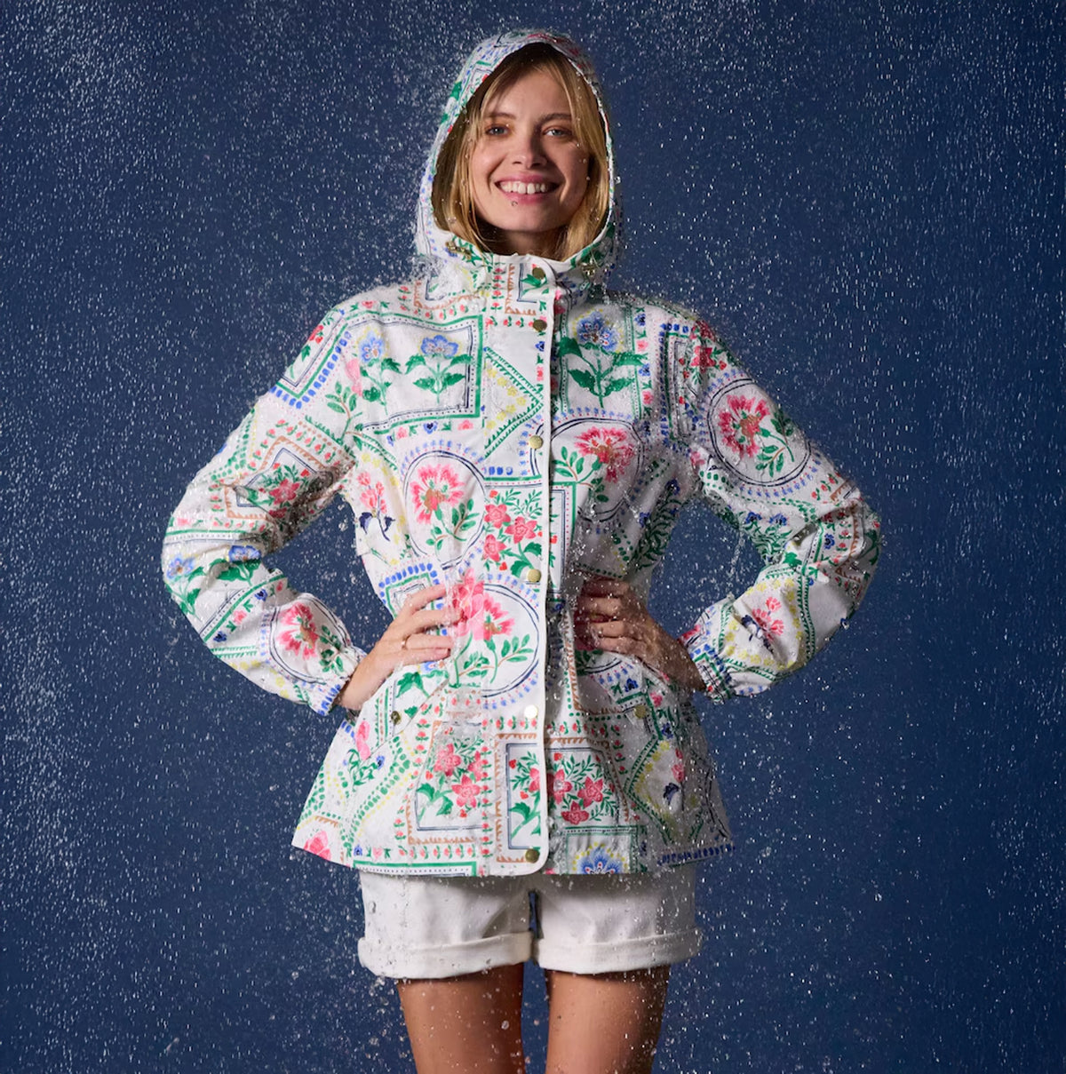 Joules Holt Womens Tile Print Waterproof Packable Raincoat with Hood, front view, model wearing in rain, vibrant floral design.