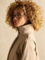 Joules Hensley Womens Waterproof Longline Coat with Packable Hood Tan Brown side view on model with curly hair and glasses.