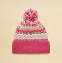 Joules KARA BOBBLE Womens Beanie Hat Pink top view with pom pom and colorful ethnic patterns on a beige background.