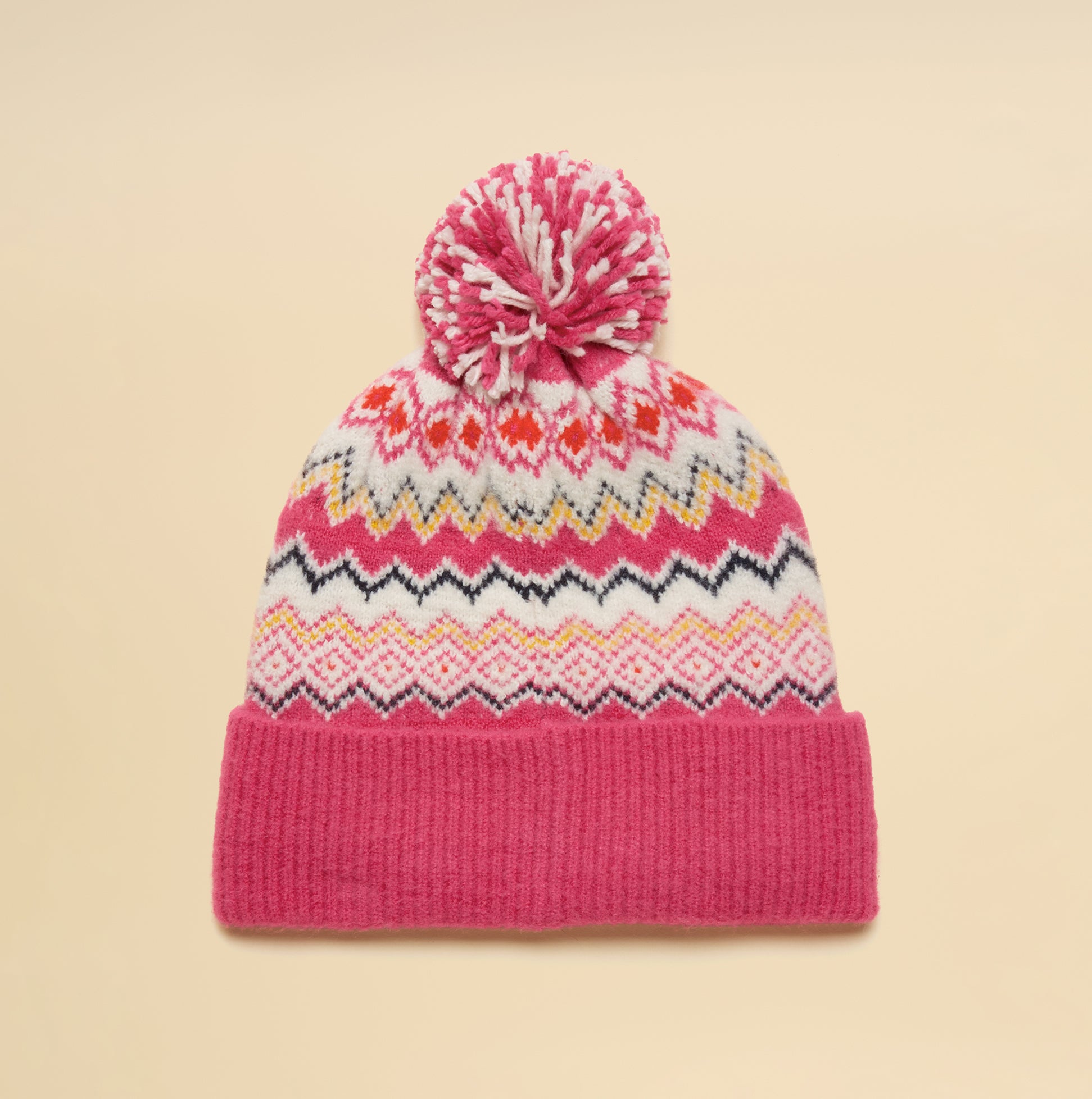 Joules KARA BOBBLE Womens Beanie Hat Pink top view with pom pom and colorful ethnic patterns on a beige background.