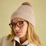 Joules EFFIE Womens Knitted Bobble Hat Camel worn by a model with glasses, close-up detail view showcasing the hat's texture.
