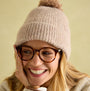 Joules EFFIE Womens Knitted Bobble Hat Camel side view on woman smiling with glasses, showcasing soft knitted texture.