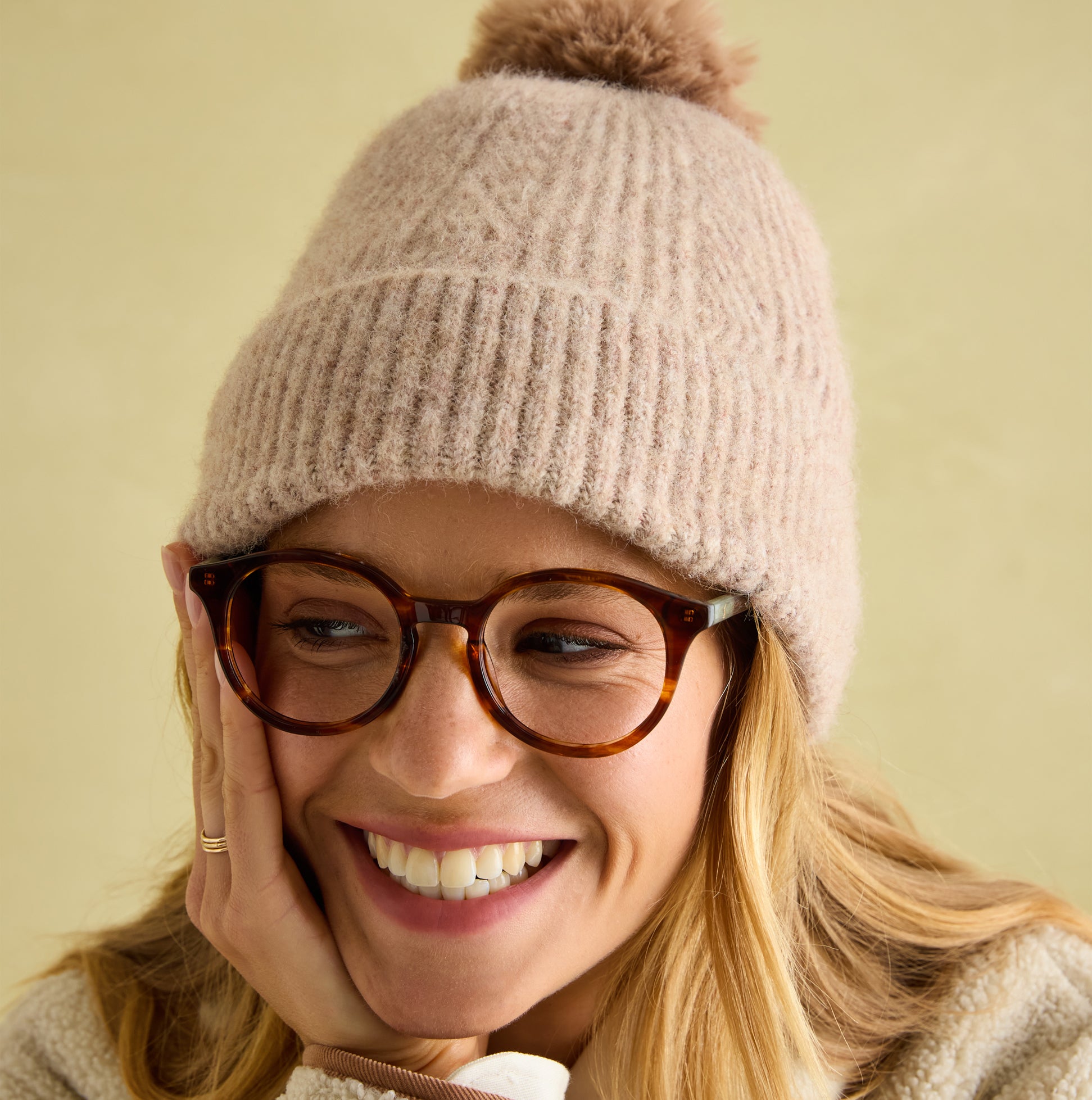 Joules EFFIE Womens Knitted Bobble Hat Camel side view on woman smiling with glasses, showcasing soft knitted texture.