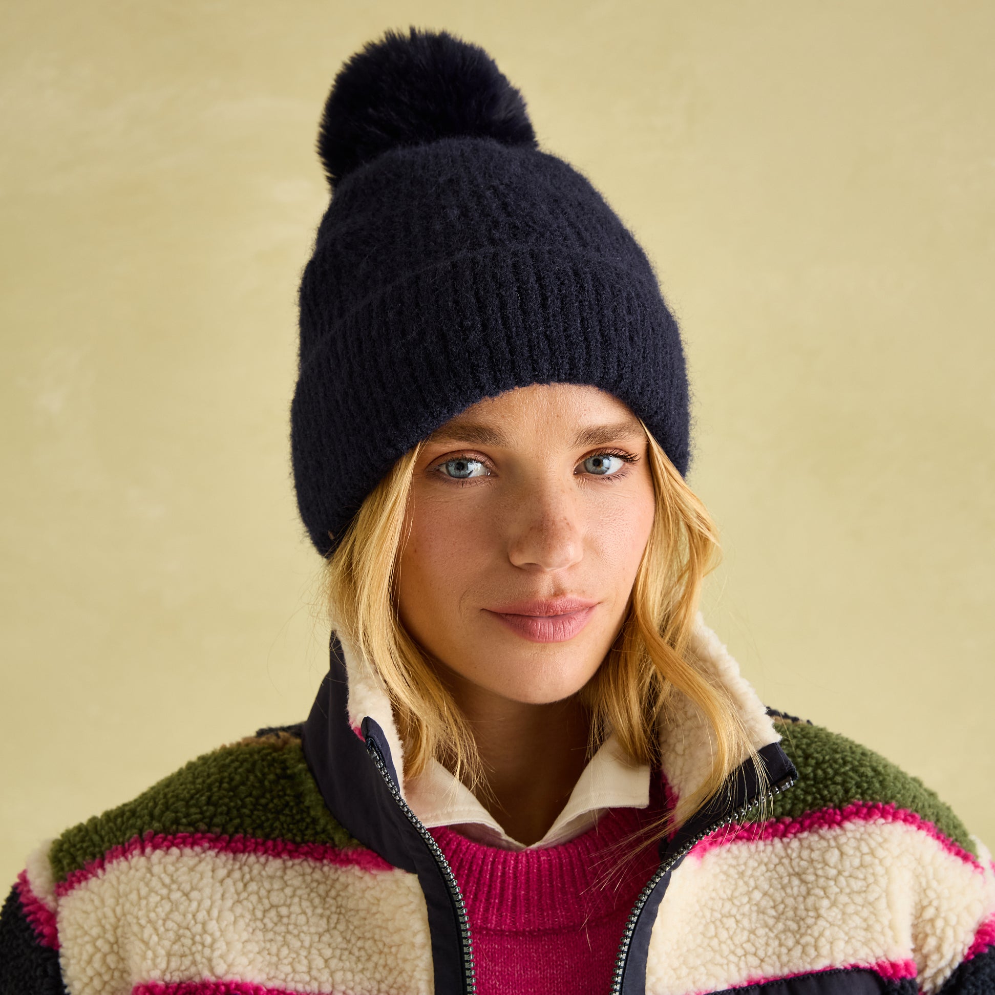 Joules EFFIE Womens Knitted Bobble Hat Navy front view worn by model with stylish outerwear backdrop.