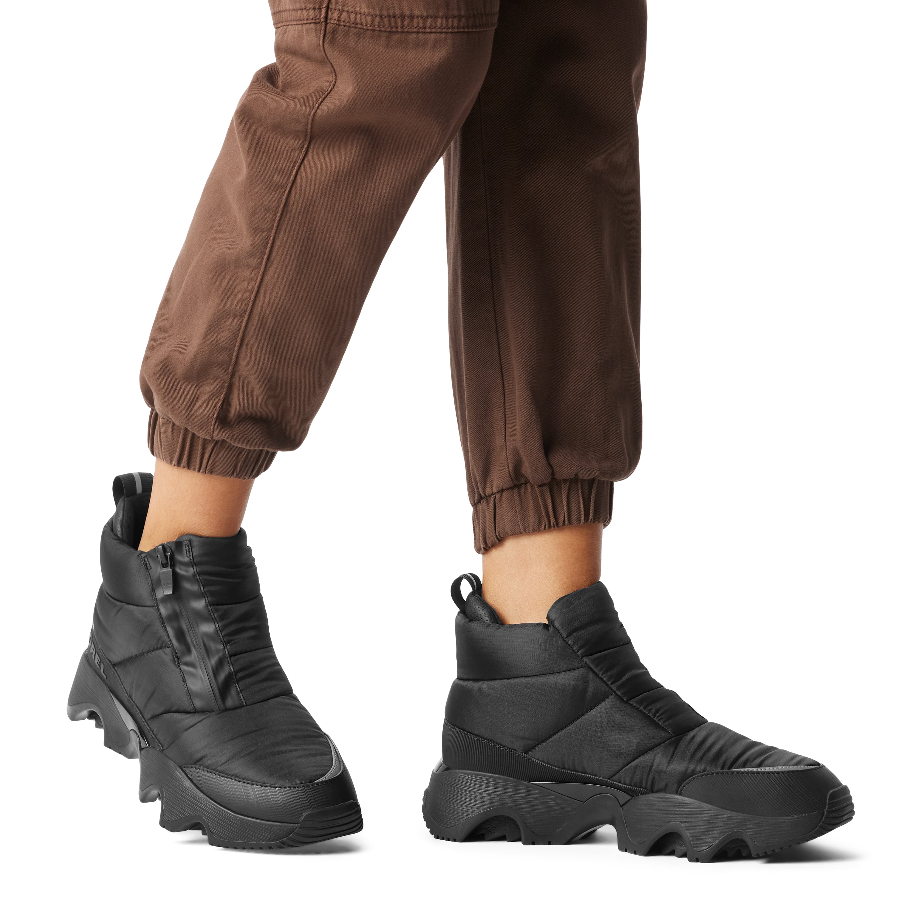 Sorel KINETIC IMPACT PUFFY ZIP Womens Winter Boots Black, side view worn with brown pants, showcasing style and comfort.