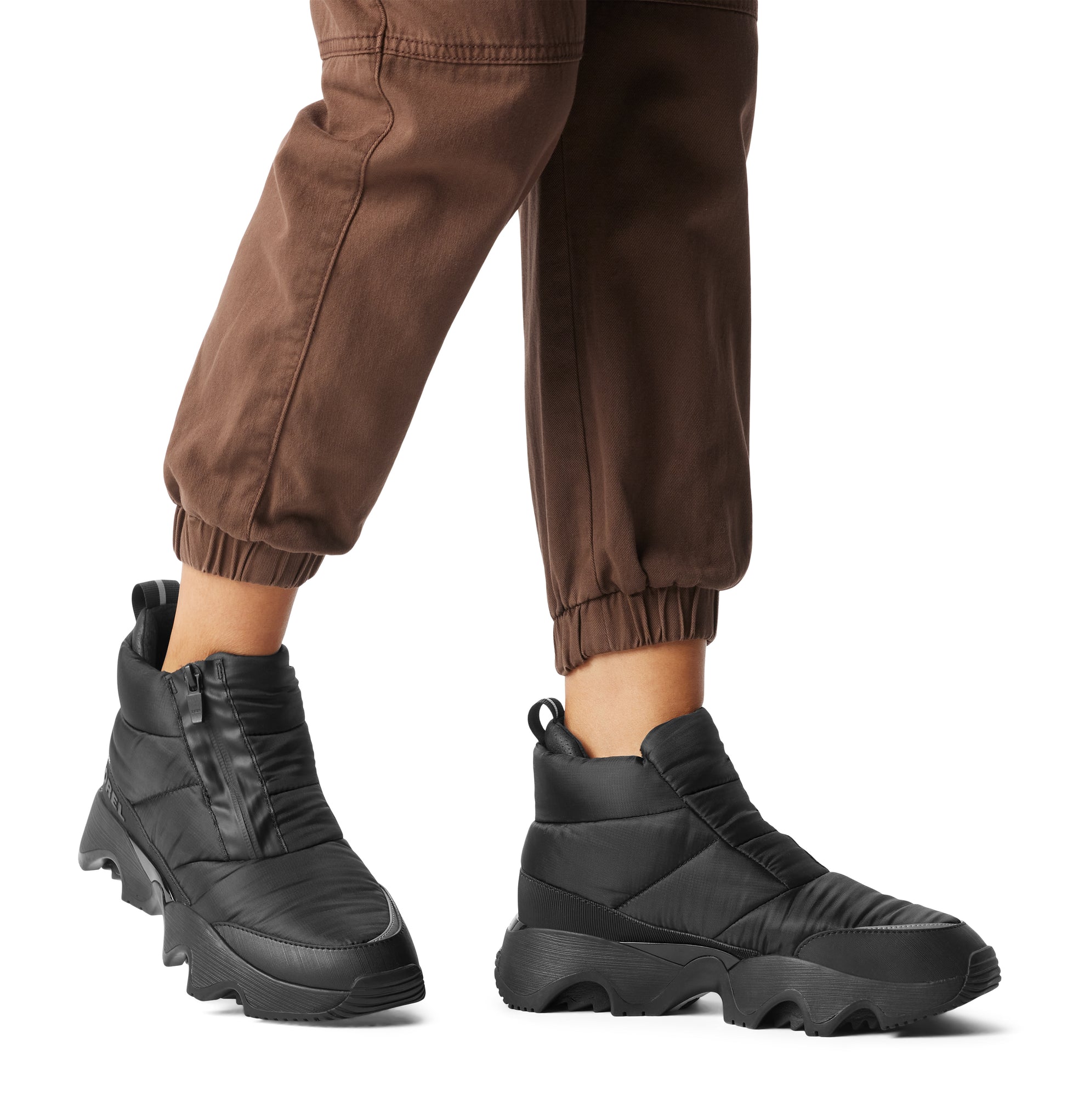 Sorel KINETIC IMPACT PUFFY ZIP Womens Winter Boots Black, side view worn with brown pants, showcasing style and comfort.