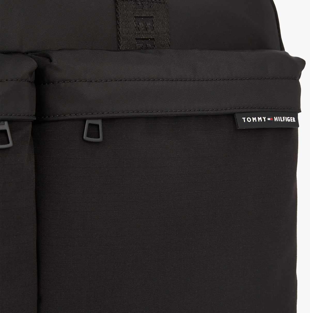 Tommy Hilfiger Rubberised Logo Laptop Bag detail view showcasing the zippered pockets and logo on a smooth black surface.