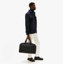 Tommy Hilfiger REPREVE DUFFLE Mens Duffle Bag Black side view on model, stylishly held in hand, casual outfit, urban setting.