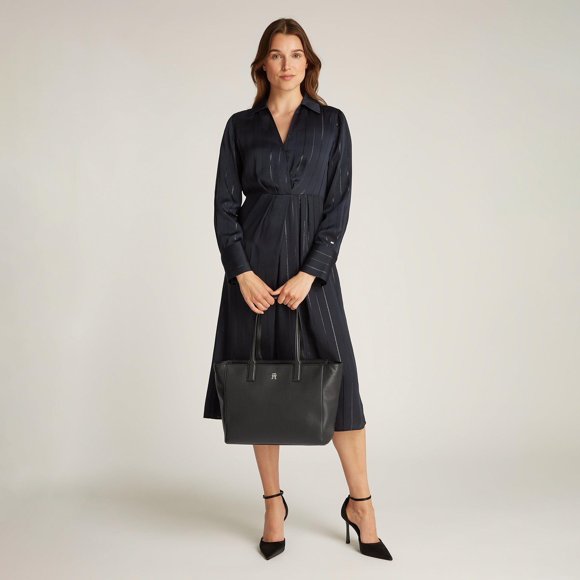 Tommy Hilfiger SOFT LOGO TOTE Womens Handbag Black held by model in a black dress, front view showcasing the handbag's zip closure and TH monogram.