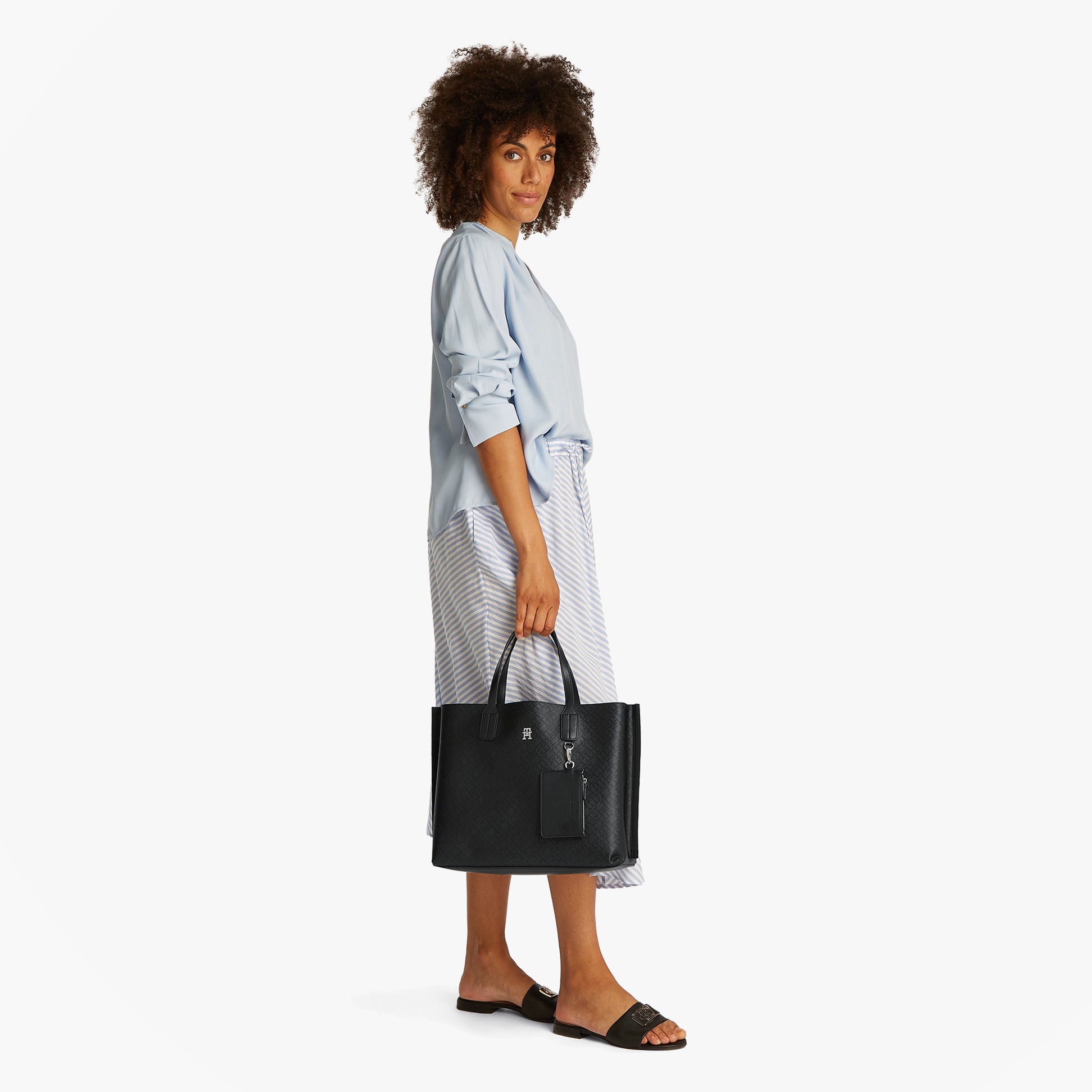Tommy Hilfiger DISTINCT SATCHEL Womens Handbag Black side view on model wearing blue shirt and striped skirt.