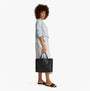 Tommy Hilfiger DISTINCT SATCHEL Womens Handbag Black side view on model wearing blue shirt and striped skirt.