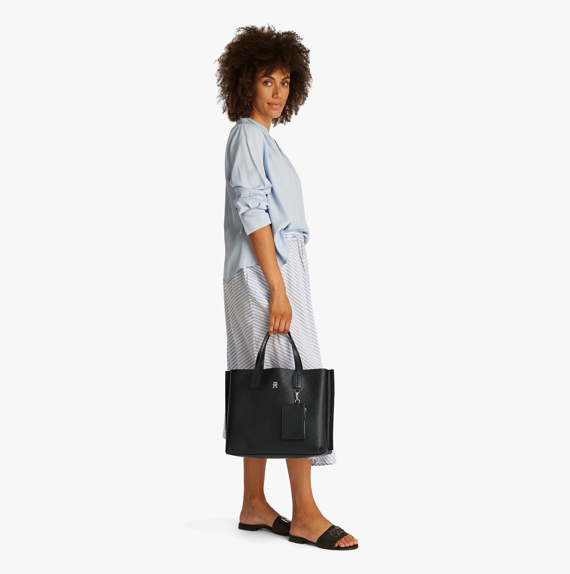 Tommy Hilfiger DISTINCT SATCHEL Womens Handbag Black side view on model wearing blue shirt and striped skirt.
