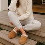 Totes Isotoner REAL SUEDE MULE Womens Slippers Tan worn by a woman sitting on steps in casual outfit.