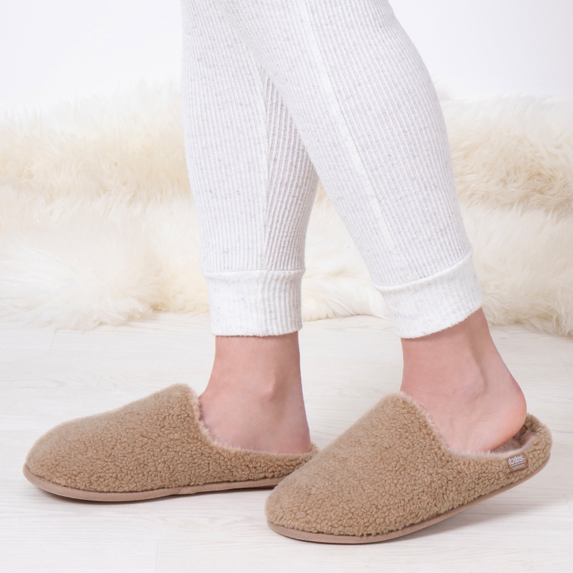 Totes Isotoner CURLY FUR MULE Womens Mule Slippers Natural side view on a model wearing white leggings.