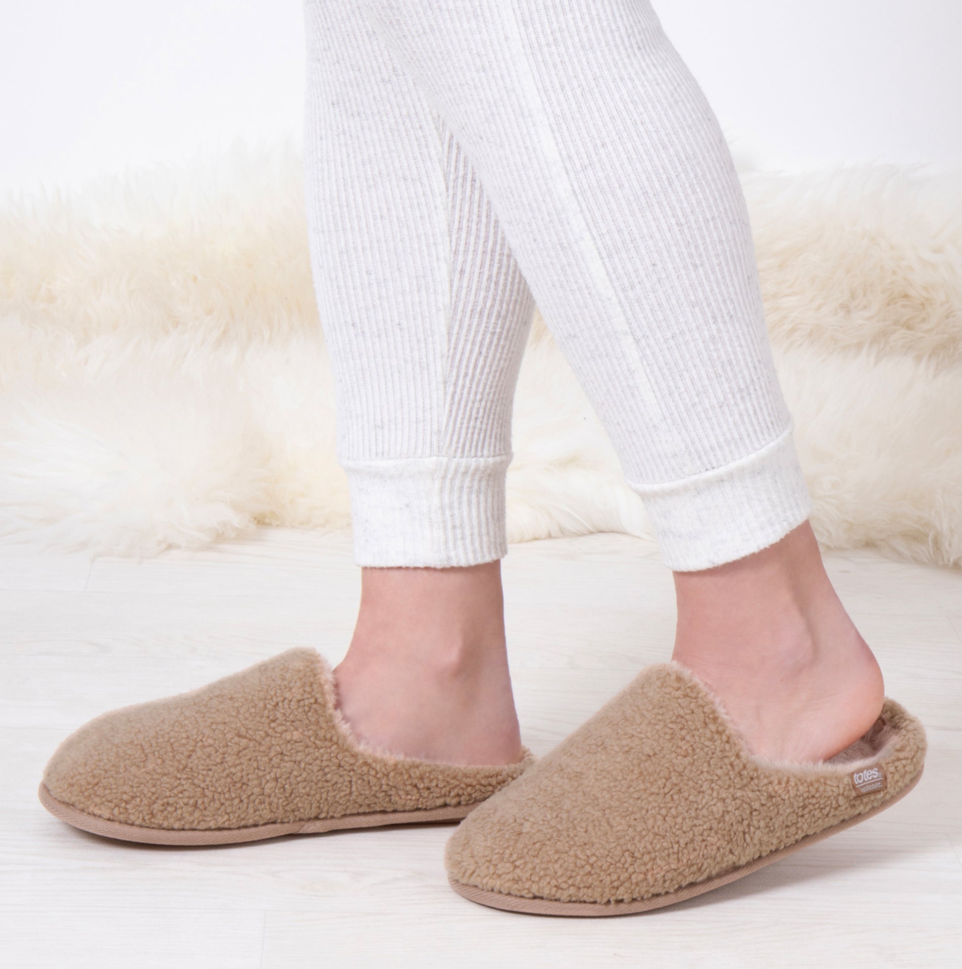 Totes Isotoner CURLY FUR MULE Womens Mule Slippers Natural side view on a model wearing white leggings.