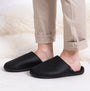 Totes Isotoner SQUARE PATTERNED SMART MULE Mens Mule Slippers Black side view on feet with beige pants.
