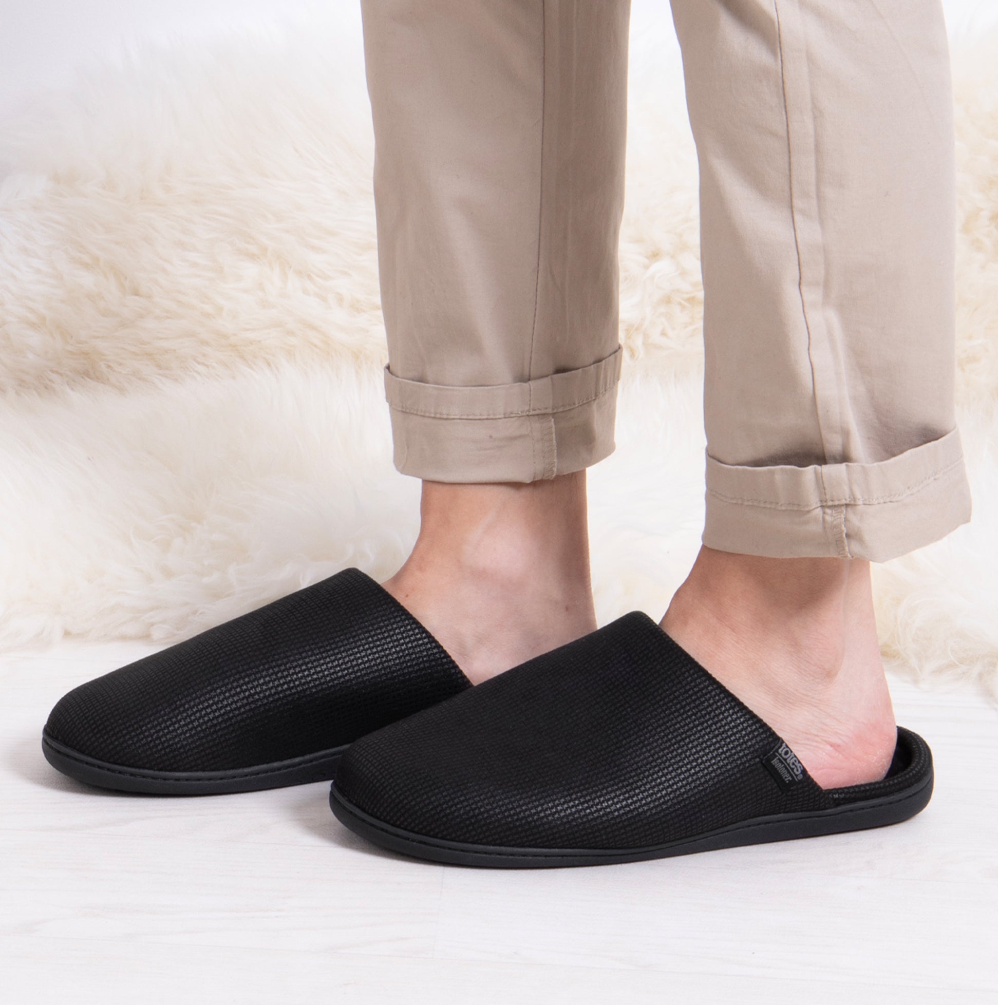 Totes Isotoner SQUARE PATTERNED SMART MULE Mens Mule Slippers Black side view on feet with beige pants.