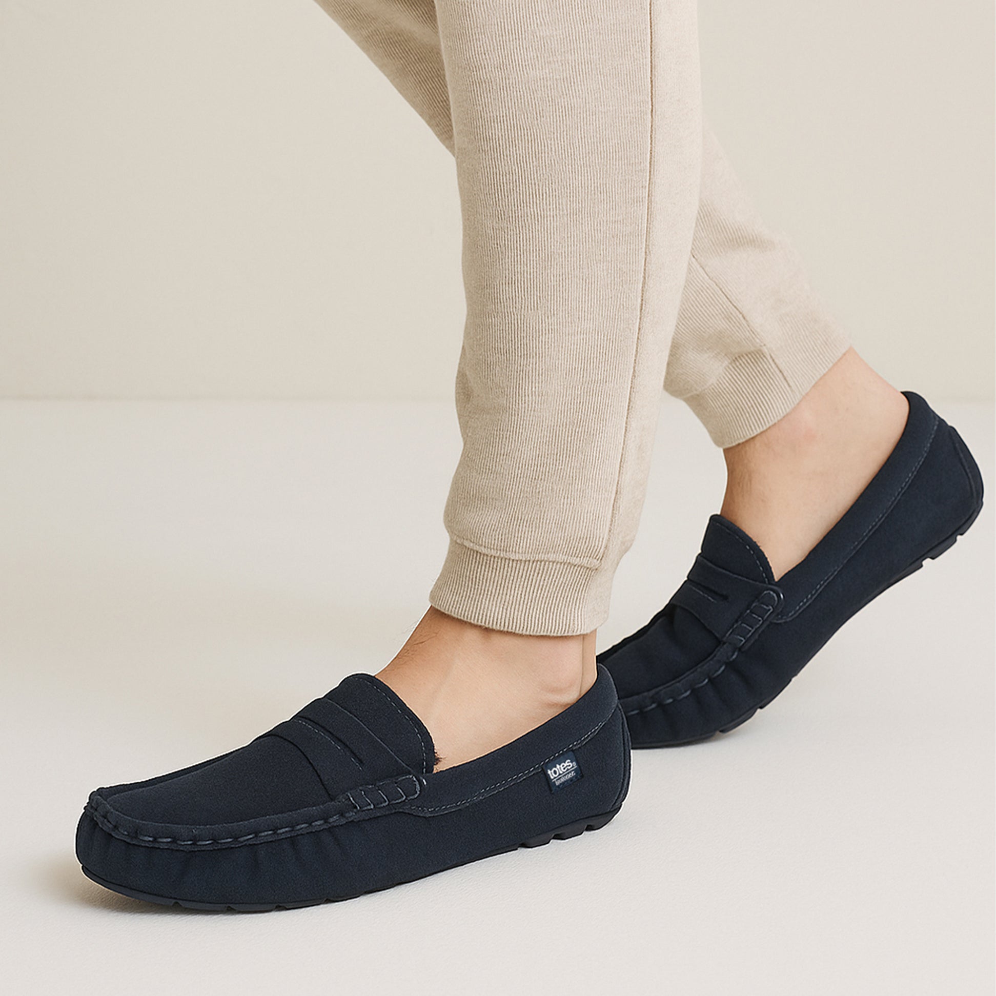 Totes Isotoner SUEDE CLASSIC Moccasin Slippers Mens Navy side view worn with light-colored pants.