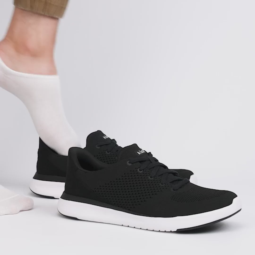 Kizik LIMA Unisex Adults Trainers Black side view with a foot wearing a sock, showcasing casual knit upper and rubber sole.