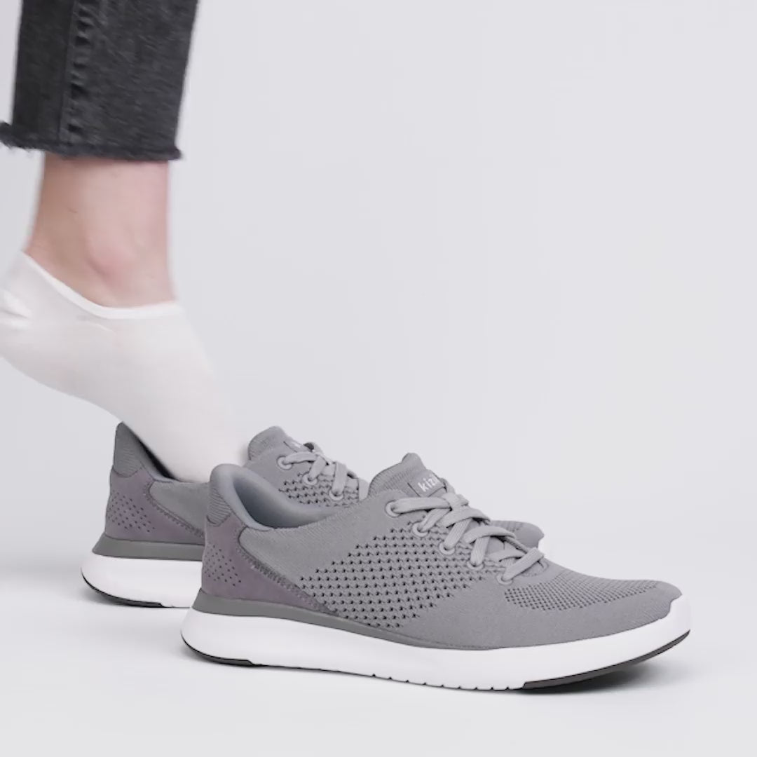Kizik LIMA Unisex Adults Trainers Grey side view with person wearing the shoes, showcasing casual knit upper and lace-up closure.